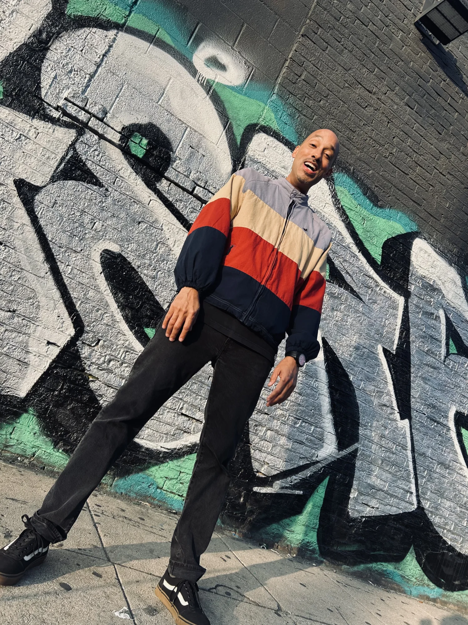 Pigeon John smiling in front of a graffiti wall